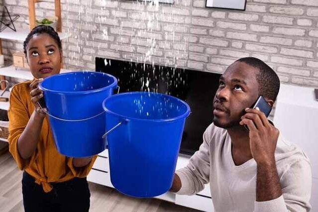 Couple with buckets catching water leaking from roof