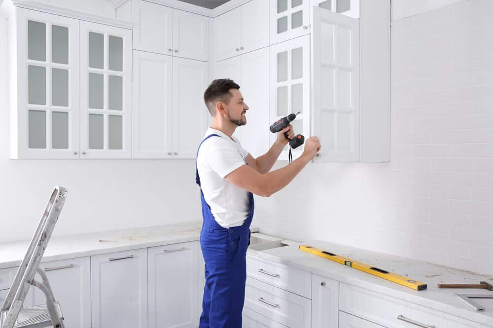 Trademan working on cabinet installations, placing handle on cabinet door with screw gun in kitchen