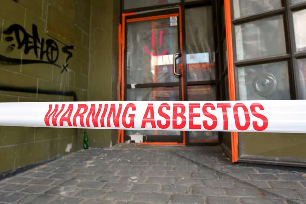 Sign reads: Warning - Asbestos removal in progress. The dangers of asbestos include serious and fatal illnesses including lung cancer, mesothelioma and asbestosis.