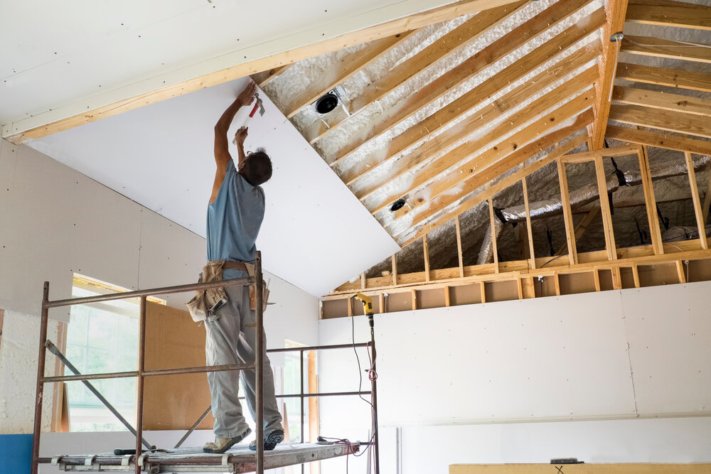 Carpentry worker putting up drywall. Hammering a nail into the sheetrock while on his tip toes.