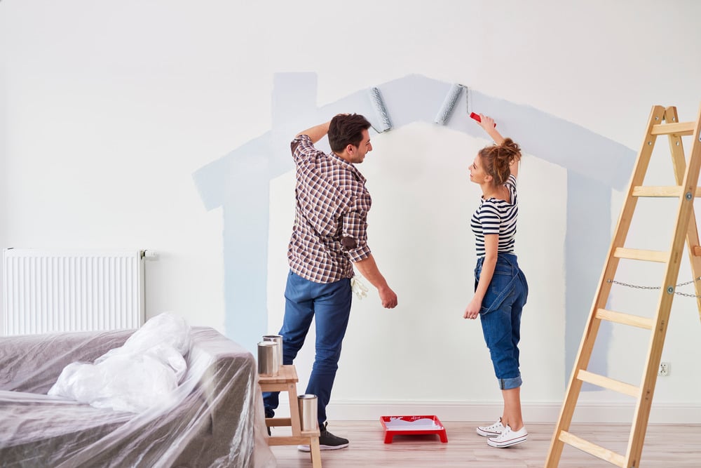 Man and woman adding a coat of new paint, the part they've done already is the outline of a house