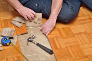 Worker removing pieces of damaged parquet. Knowing whether to repair or replace damaged flooring is important for homeowners