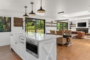 Kitchen in open concept home with view of living and dining rooms. Interior is white and bright due to skylights.